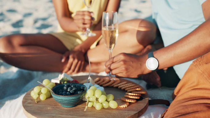 野餐，酒和夫妇的手在海滩上香槟吐司为周年纪念，爱情和约会。大自然，美食与人们一起畅饮，节日里有水果和