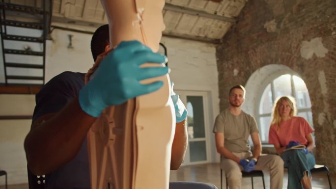 特写镜头:一名身穿蓝色医疗制服、戴着手套的黑人男医生正在展示一个正在为公众进行医疗培训的人体模型。医