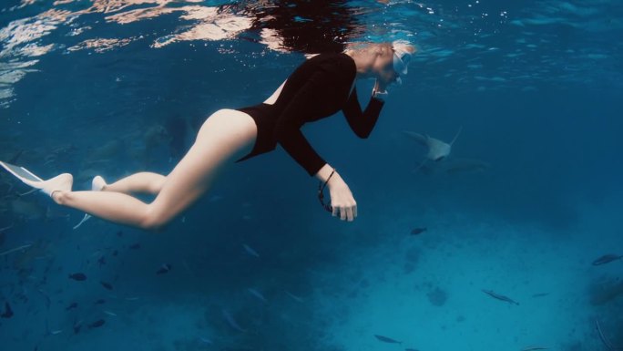 在马尔代夫，一名女子自由潜水者在海面上休息，然后潜入热带蓝色大海的深处