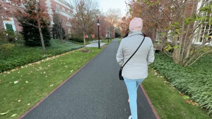 一个女人独自走过哈佛大学的花园和建筑