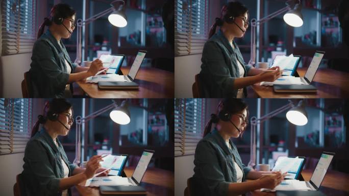年轻的亚洲女性坐在黑暗的客厅里，戴着耳机在笔记本电脑上进行视频会议