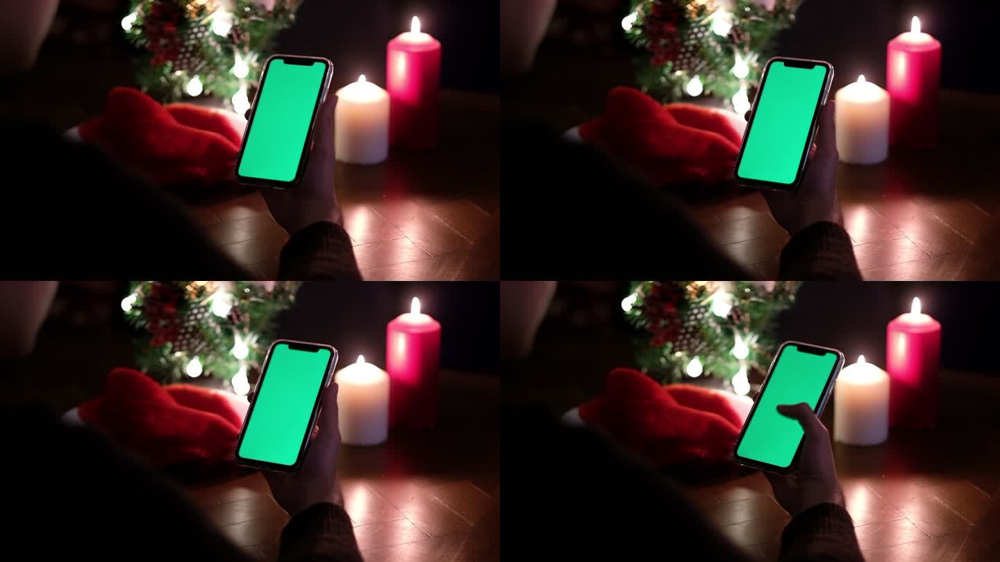 使用绿屏的智能手机，夜晚的圣诞树和蜡烛