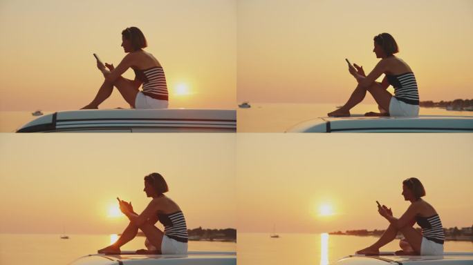 在日落时分坐在露营车顶部使用手机的女子的慢镜头