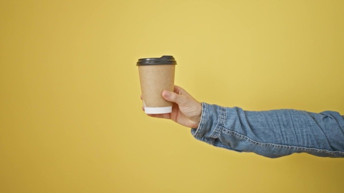 一个人伸出手臂，在纯黄色的背景下，拿着一个一次性咖啡杯，重点是休闲的生活方式。