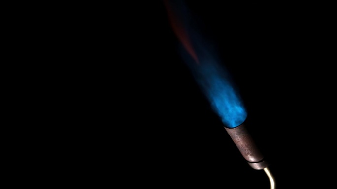 燃气燃烧器火焰。黑色背景上孤立的蓝色火焰，特写。蓝色火焰从燃气火炬的喷嘴打开。手动丁烷燃烧器火焰。视