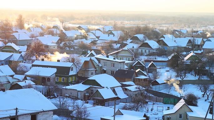 在一个寒冷的冬日早晨，在太阳的映衬下，烟囱里冒出橙色的烟雾，白雪覆盖的村庄房屋。美丽的冬季大自然。文