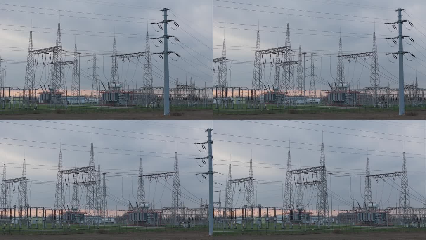 夕阳的云朵勾勒出无人机在地面上捕捉到的变电站。高压电线杆、晶格结构、电缆和变压器的复杂排列增加了视觉