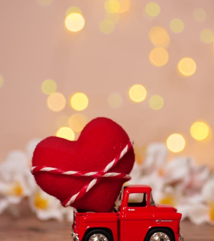 红色卡车，后面有一颗大红心，用来送情人节的爱，粉色背景，模糊的白色花田，散焦闪闪的散景光，垂直镜头