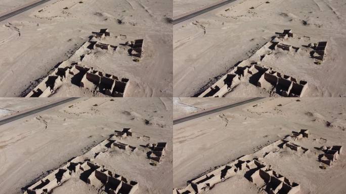 在干燥的沙漠景观中，相机缓慢地盘旋在破旧的泥砖土坯建筑上，天空湛蓝，没有云