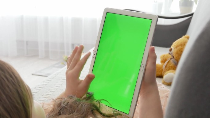 一个女孩躺在沙发上，手里拿着一个绿色镀铬屏幕的平板电脑。看电子游戏或看书。无线技术和互联网的概念