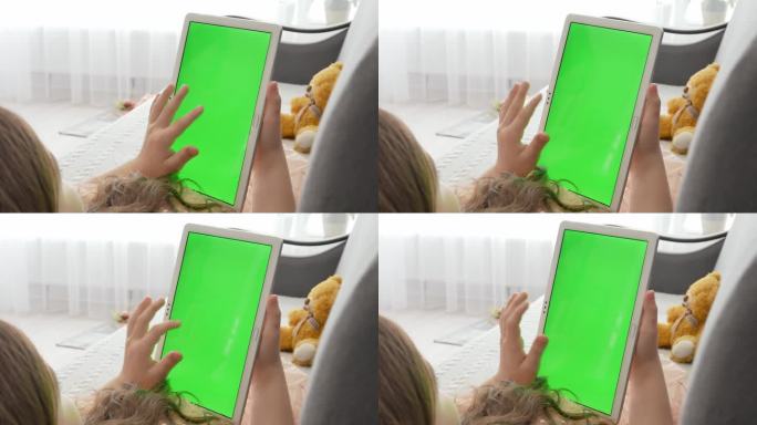 一个女孩躺在沙发上，手里拿着一个绿色镀铬屏幕的平板电脑。看电子游戏或看书。无线技术和互联网的概念