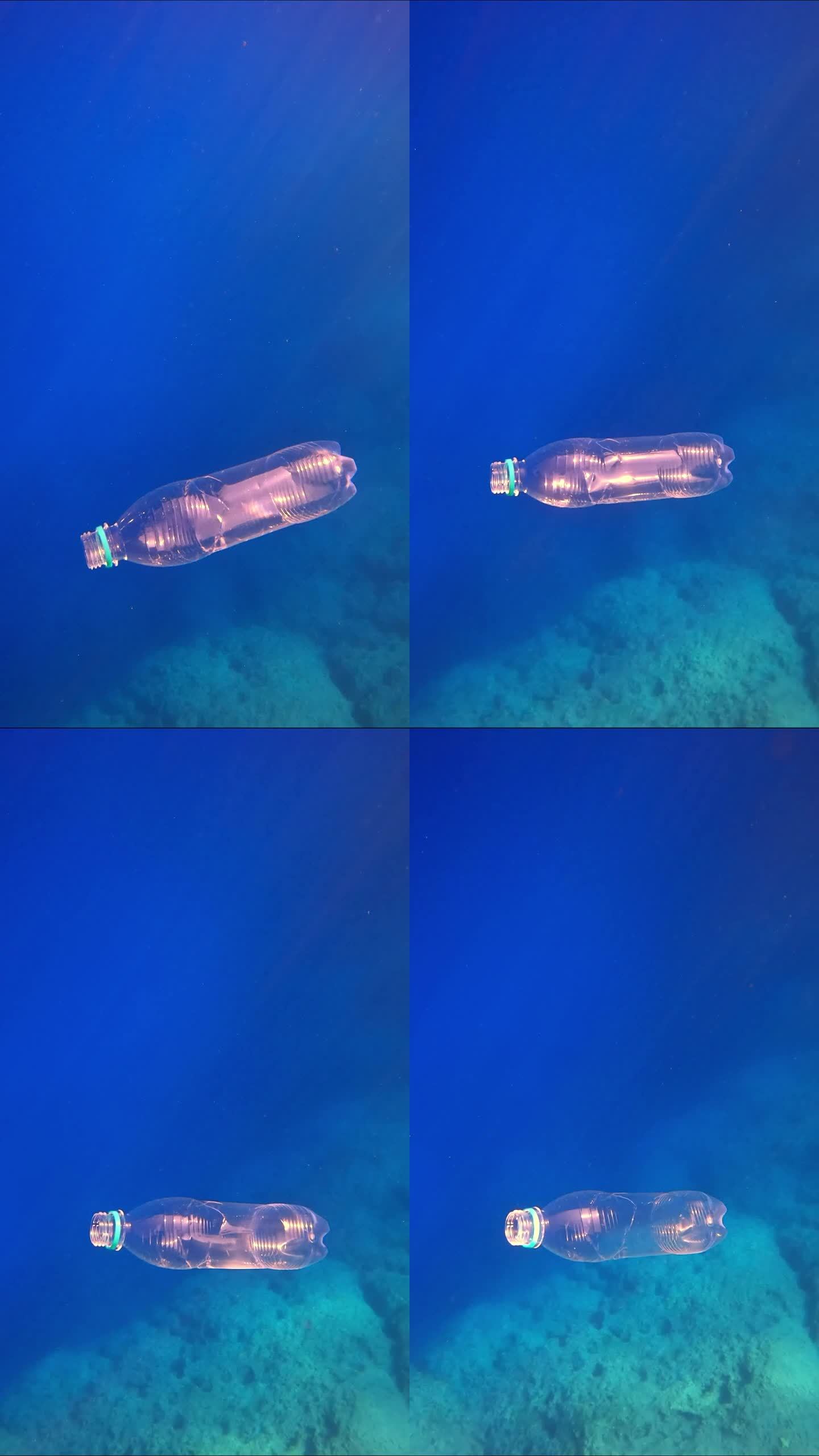 透明的一次性塑料瓶在蓝色的海水中下沉到岩石海底