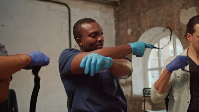 特写镜头:一名身穿蓝色医疗制服的黑人男医生在急救训练中演示了一种医疗安全带，即在手臂上系紧医疗带的技