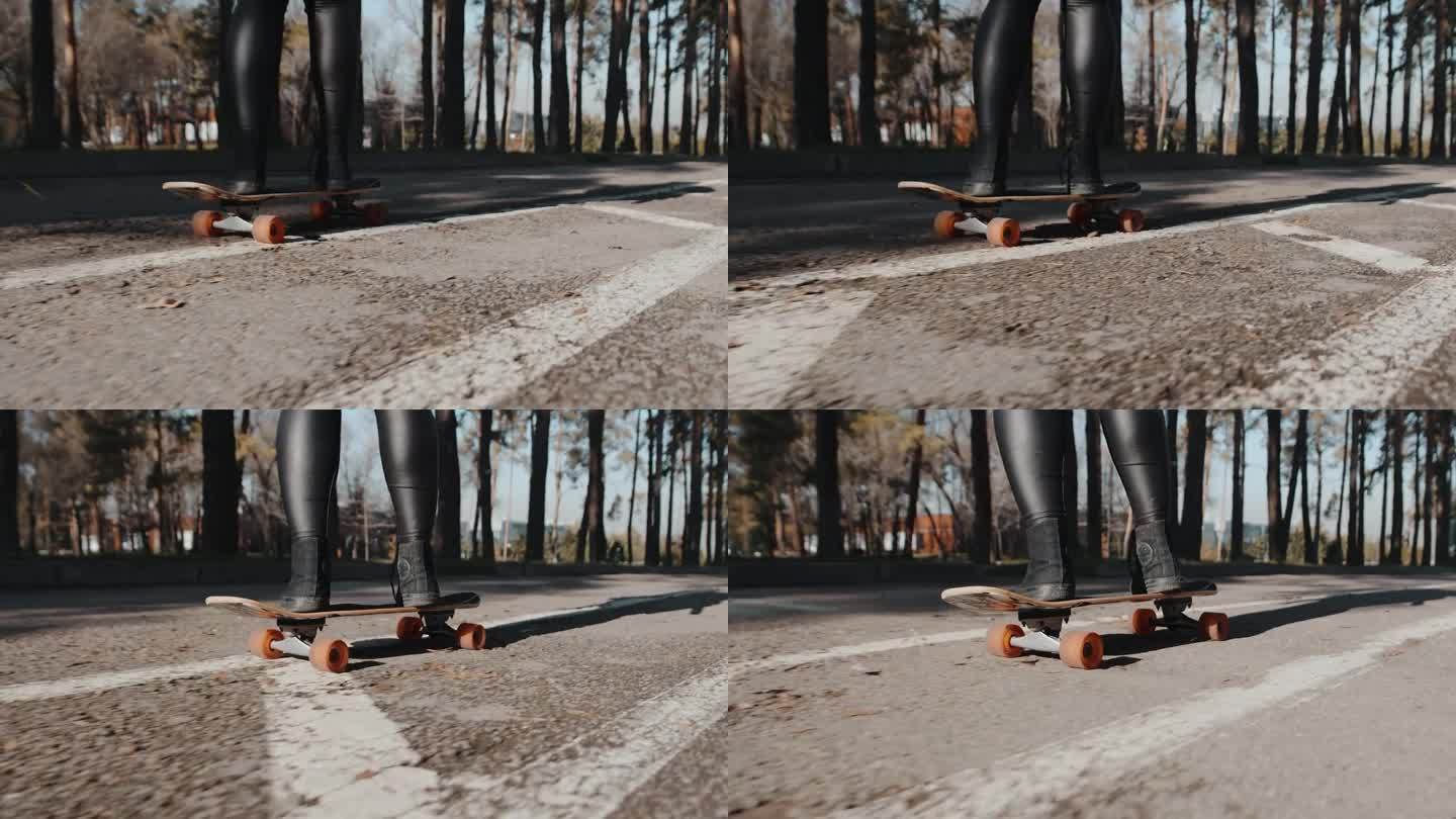 一个阳光明媚的日子里，一个小女孩在城市公园的柏油路上熟练地滑着滑板疾速前进的特写，后视图。有趣的秋季