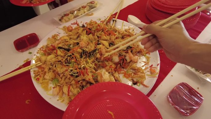 春节庆祝活动期间，人们用筷子从一盘鱼生中取出食材，繁荣地将生鱼沙拉放入红色塑料盘子中