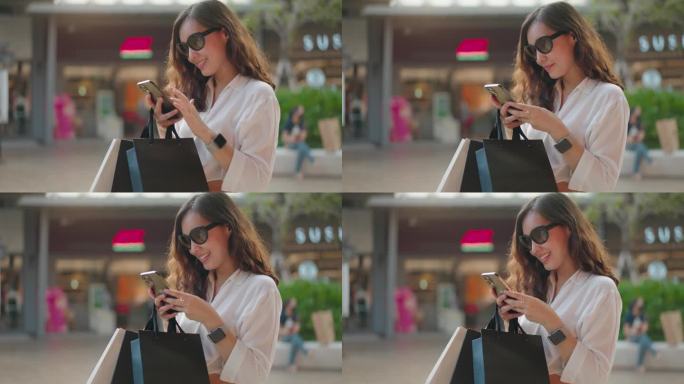 亚洲女顾客手持购物袋在商场使用手机