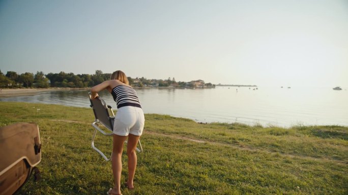 女子从湖边露营车里搬椅子的慢镜头