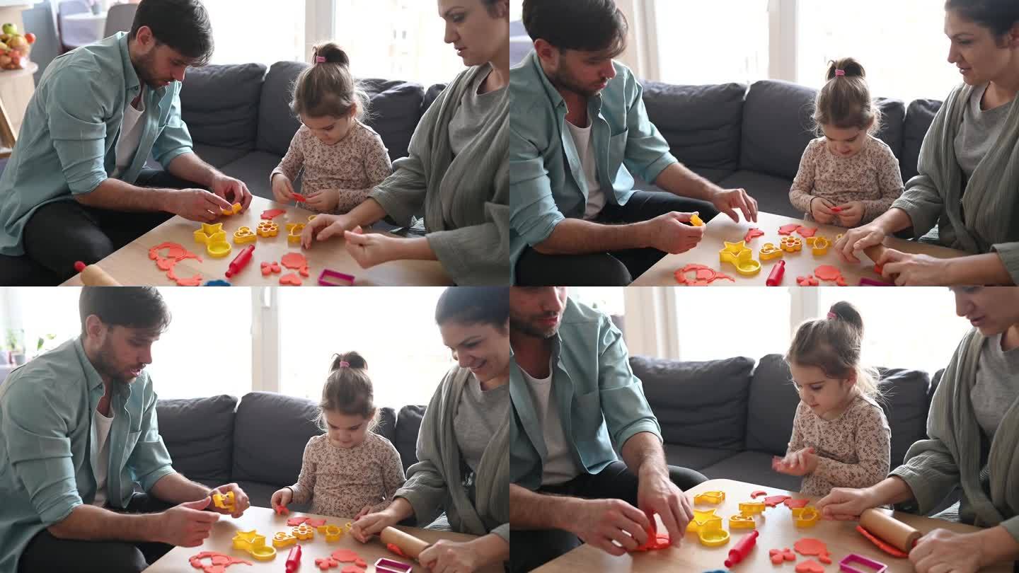 父母和女儿在家里玩粘土。一个小女孩正在用橡皮泥做造型的家庭