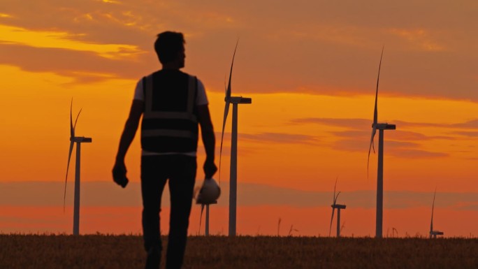进展的剪影:工程师接近风力涡轮机。清洁能源。拥有风力涡轮机的绿色能源农场。