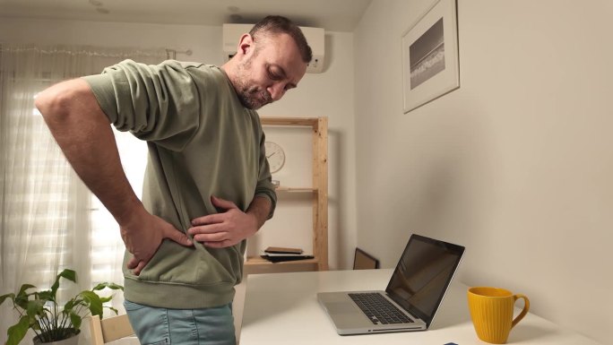 一个人在用笔记本电脑工作时背部疼痛。