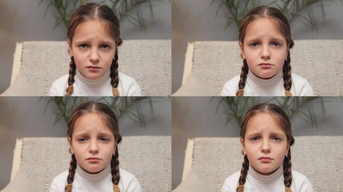 小女孩不开心穿着白色高领毛衣扎着小辫儿坐在沙发上对着镜头生气准备哭被冒犯了