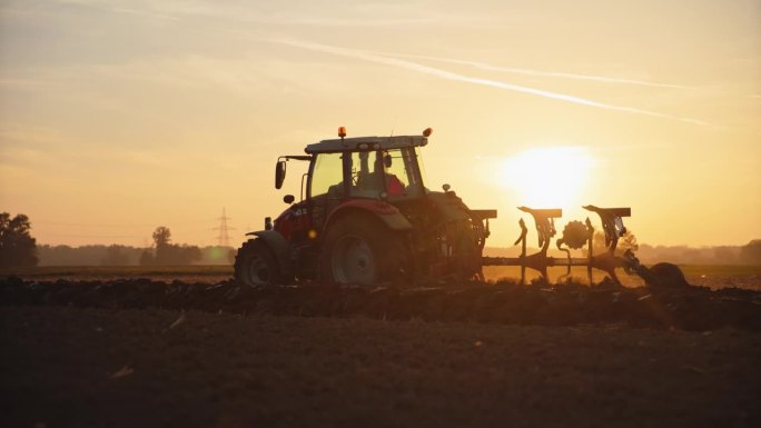 日落时分，男农民在拖拉机上对着天空耕作有机农场