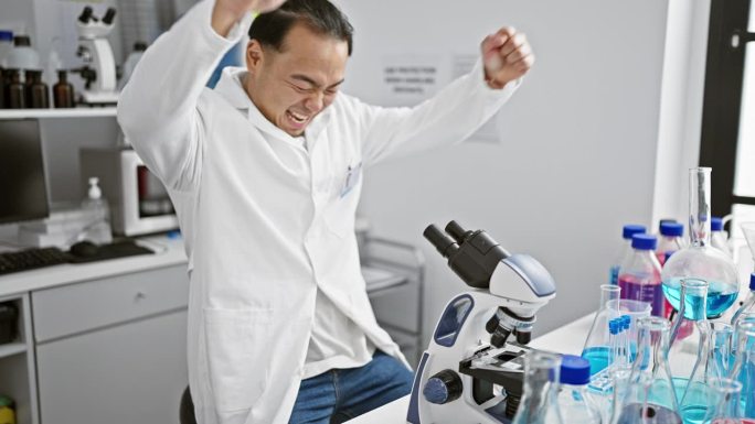 微笑的中国年轻科学家在实验室用显微镜庆祝重大发现，体现了医学研究的胜利精神