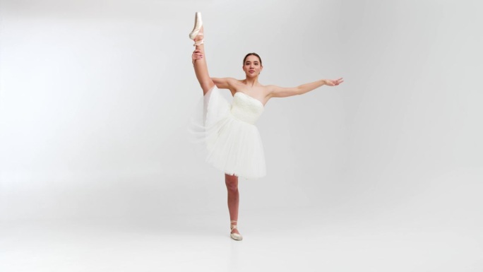 一位身穿白色芭蕾舞裙的专业芭蕾舞演员在一个大型训练大厅里跳舞。一个女孩穿着戏服跳舞。在一个宽敞的摄影