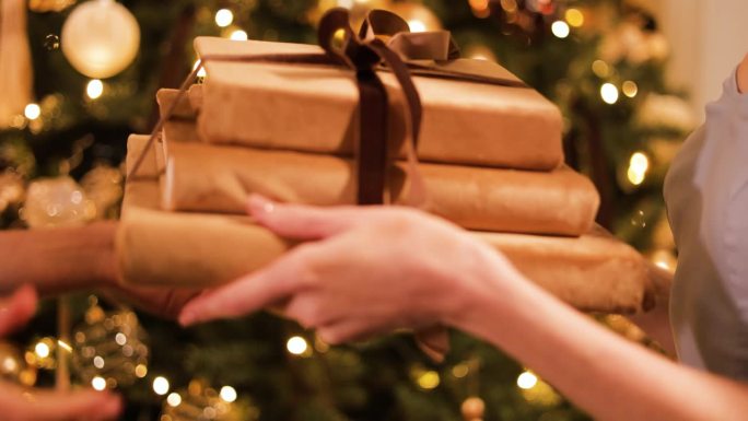 以装饰过的冷杉树为背景，妇女赠送和接受圣诞礼物的特写。女士穿着时髦的晚礼服，用丝带把一摞书送给她最好