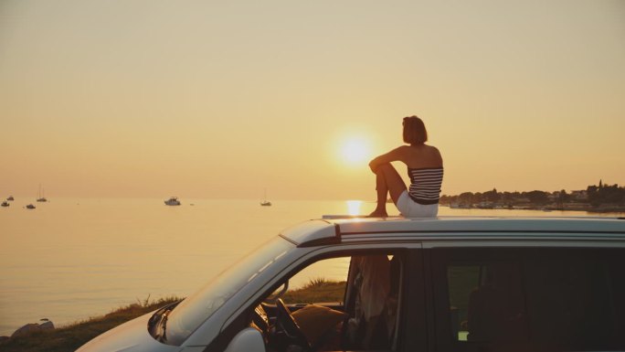 在日落的时候，女人坐在海边的露营车上，对着天空