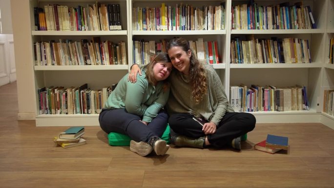 有特殊需要的中年妇女和老师在图书馆拥抱的肖像