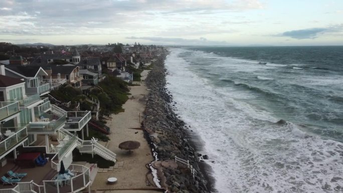4K鸟瞰图无人机拍摄的南加州一个城市海滩海岸线，蓝色的太平洋，海浪涌进来，海滩上有漂亮的房子，强风正