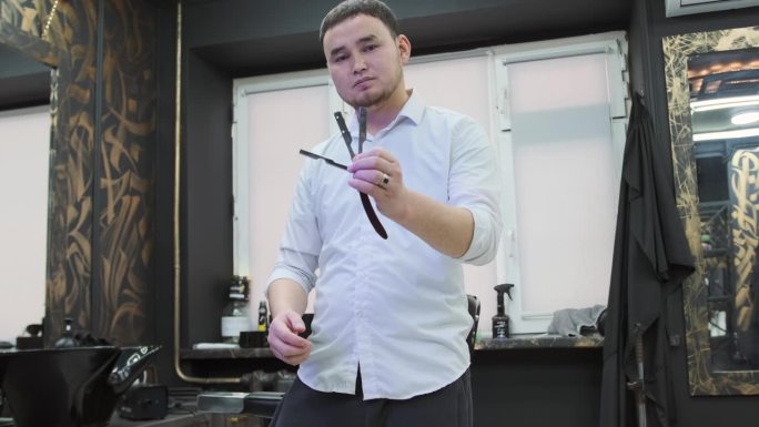在理发店里，一位亚洲美发师正在展示一把直刀。