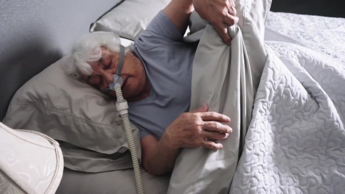 患有睡眠呼吸暂停的老年妇女睡在床上，戴着CPAP(持续气道正压通气)机来帮助她入睡