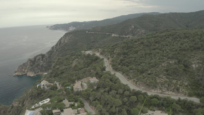 无人机拍摄的两辆跑车行驶在漫长曲折的山路上，在一个灰色的一天在意大利的一个湖泊或海洋附近