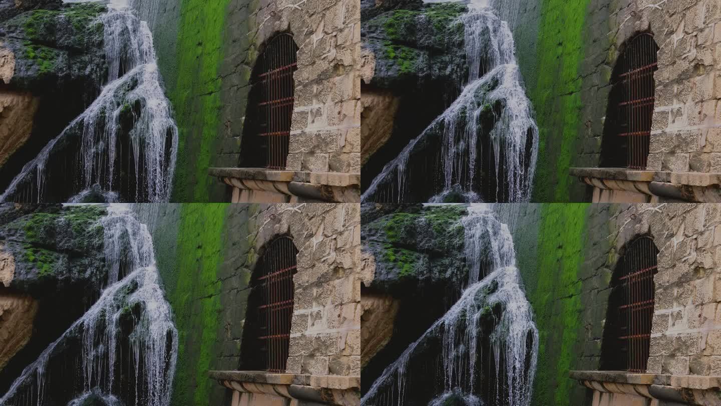 在这个迷人的慢动作视频中，一个特写的瀑布在中世纪的墙壁旁边流淌，门上有栅栏。