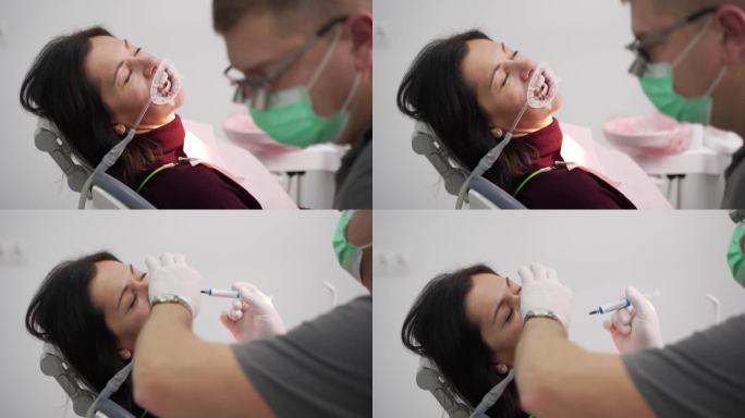 现代牙科诊所中，男牙医用双筒望远镜治疗女病人的牙齿。在安装贴面之前，医生用注射器将蓝色蚀刻凝胶涂在牙