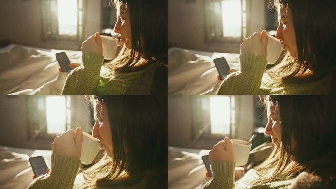 早上躺在家里的床上，一边刷智能手机一边喝咖啡的微笑年轻女子的特写侧视图