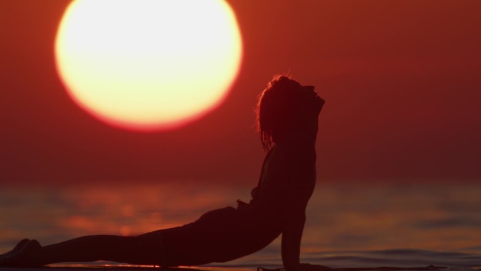 宁静的女人练习瑜伽在海上冲浪板在日落时的慢镜头