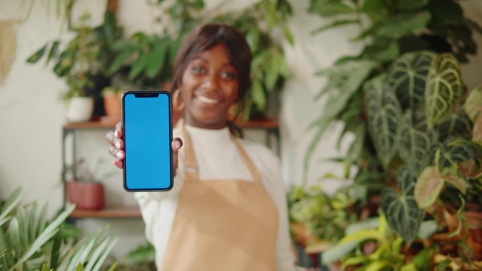 第一个非裔美国女人拿着带色度键的手机。微笑的温室工人女植物学家，小企业主。园丁在花店，植物店工作。