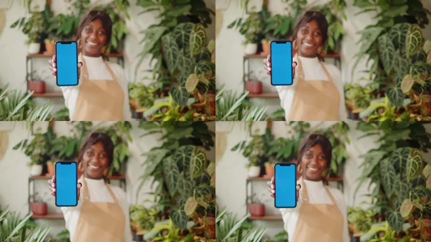 第一个非裔美国女人拿着带色度键的手机。微笑的温室工人女植物学家，小企业主。园丁在花店，植物店工作。