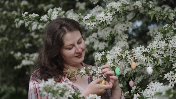 一位白人妇女用装饰蛋装饰盛开的春树。