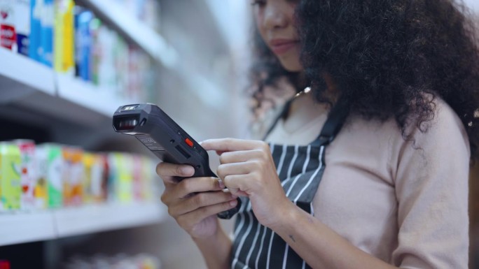 年轻女子在超市用条码扫描器检查货架上的商品。