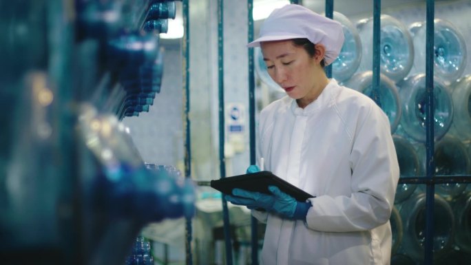 在一家工厂里，一名穿着实验室服装的女工拿着药片检查水瓶的生产。瓶装水生产中的HACCP体系