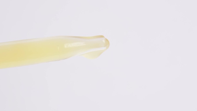 一滴黄色血清从玻璃移液管中落下，近距离观察。油提取物从玻璃移液管中滴下