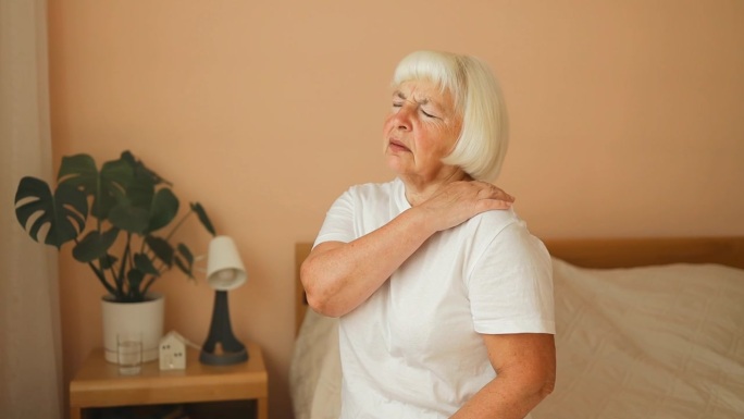50多岁的女人肩膀疼，穿着睡衣坐在床上。老妇人忍受着剧痛。