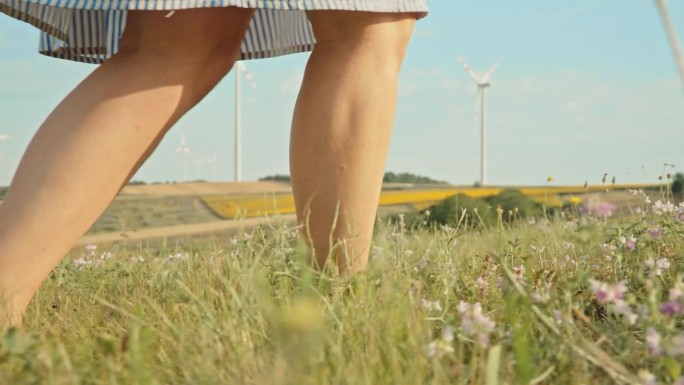 一个不知名的女人赤脚走在草地上，沿着风力涡轮机