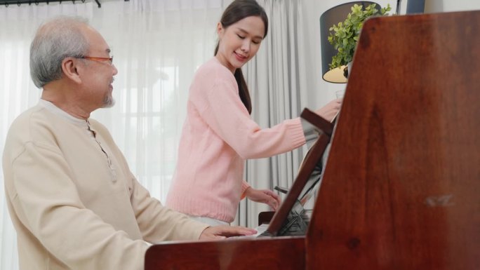 家庭。年轻的女子为年长的男子教钢琴，快乐的女儿和年迈的父亲戴着眼镜在家里的客厅里放松地一起弹钢琴，过