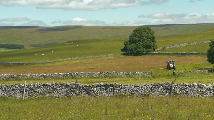 在美丽的英国乡村，用拖拉机在石墙牧场上割草