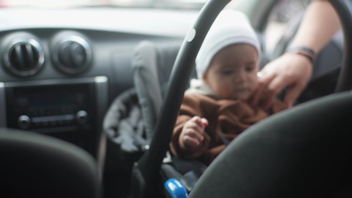 特写:无法辨认的女性双手系紧婴儿安全带，男婴坐在前座背对引擎。车内系着安全带的可爱孩子。